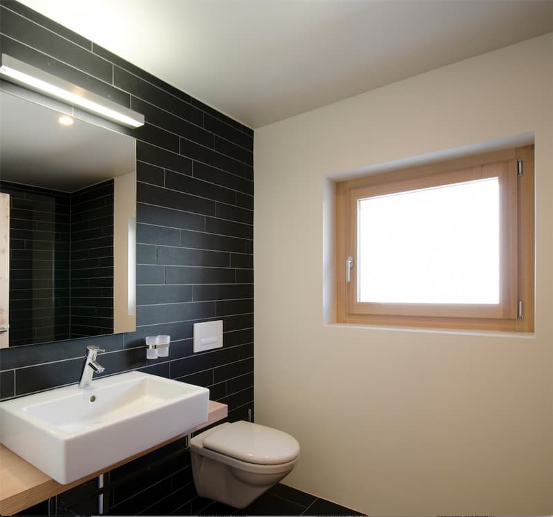 Bathroom: white sink, white toilet, mirror, white tiled wall, wooden window frame