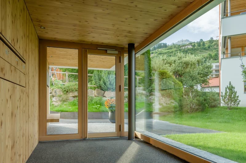 wooden walls, glass sliding doors, paved pathway, flower pot, lush green grass, mountains in the distance