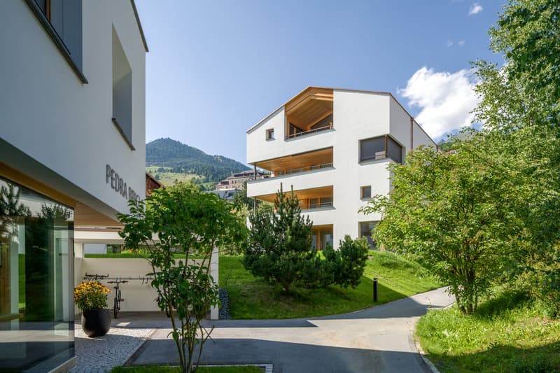 Modern white building with balconies, raised ground floor, bicycles parked in front