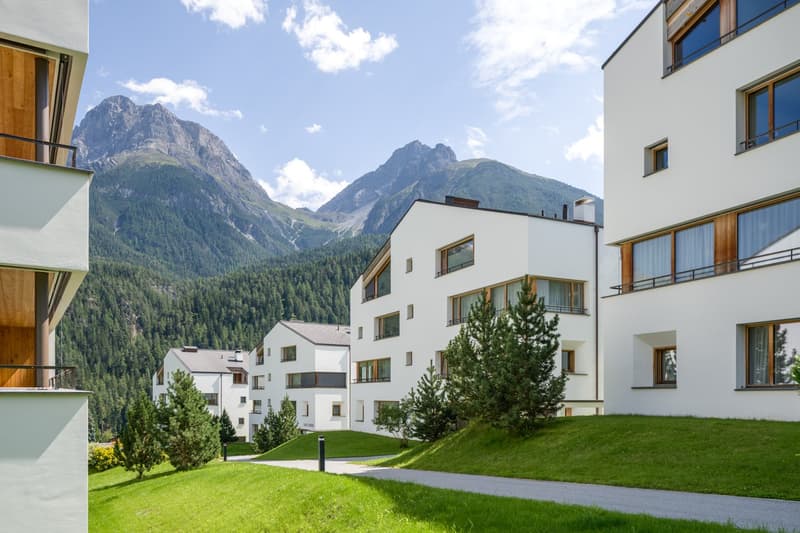 Multiple white apartment buildings, balcony, greenery, mountain in the background