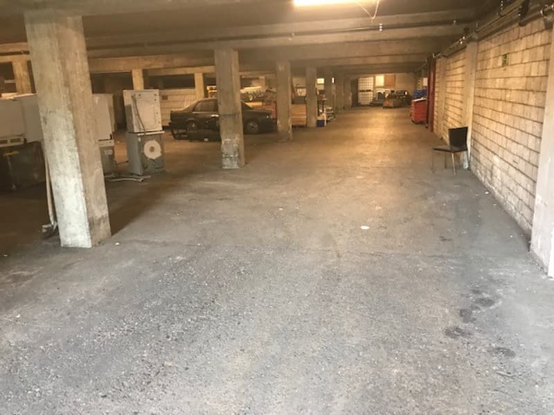 underground parking lot, multiple columns, one car parked, storage boxes on the wall
