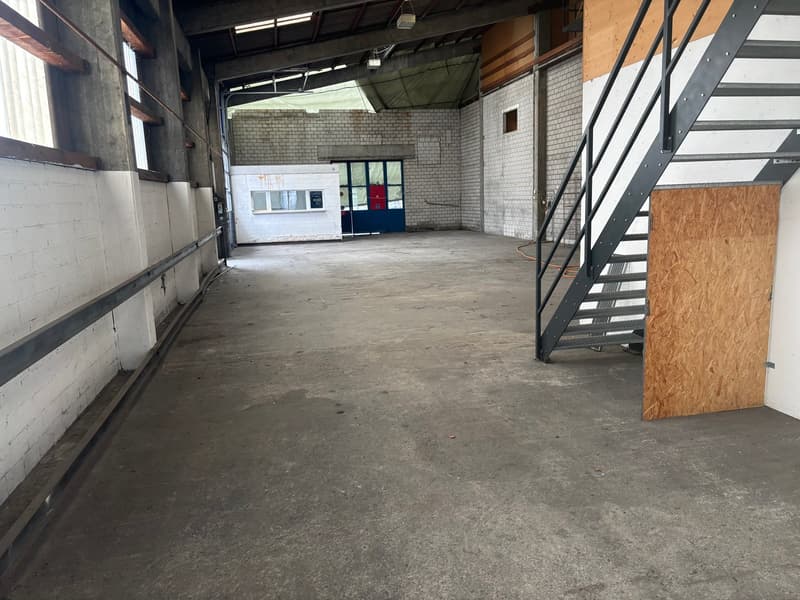 spacious warehouse, concrete floor, white brick walls, metal stairs, two large doors, large windows, lights hanging from the ceiling