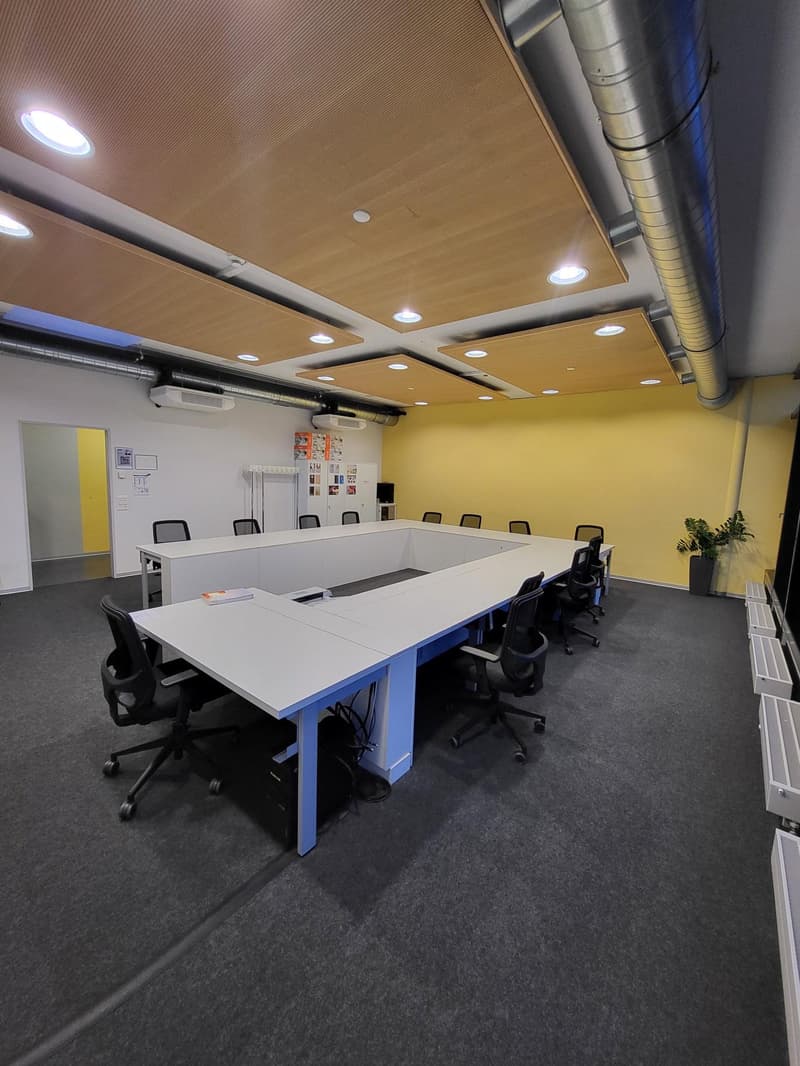 Large conference room, long white tables, black rolling chairs, white walls, yellow walls, ceiling lights