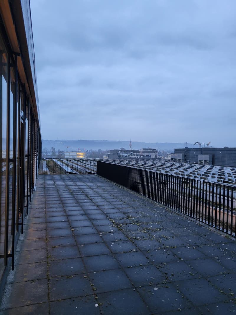 Exterior view of a rooftop terrace with a view of the city, a metal railing, and tiled flooring.