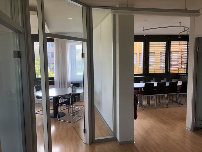 modern office room with wooden floors, glass partitions, tables, chairs, large windows with blinds