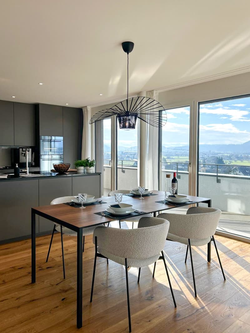 a modern and open dining room with a table and chairs, large windows with balcony access, a wooden floor, and a pendant light, a view of a valley