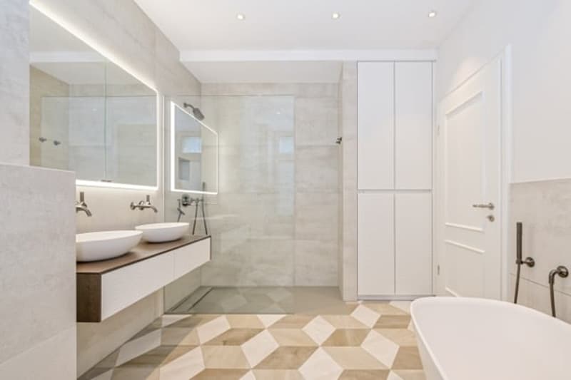 Modern bathroom with two sinks, a large mirror, a bathtub, a glass-enclosed shower, and white cabinets.