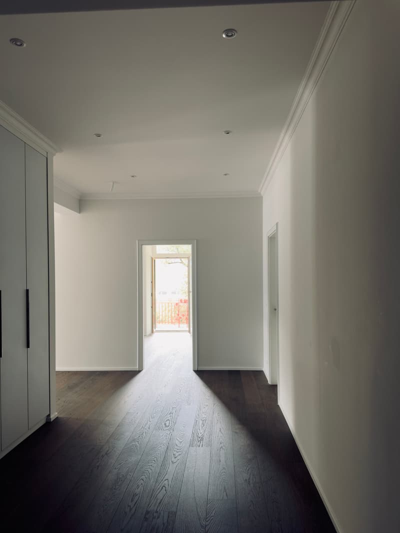 Empty room with wooden floor, white walls, two doors, open doorway to balcony