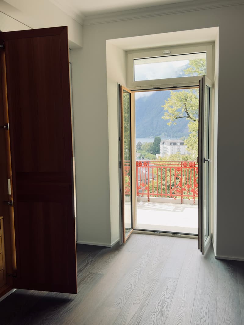 door open to balcony, balcony with red railing, wooden floor, white walls, view of mountains and trees