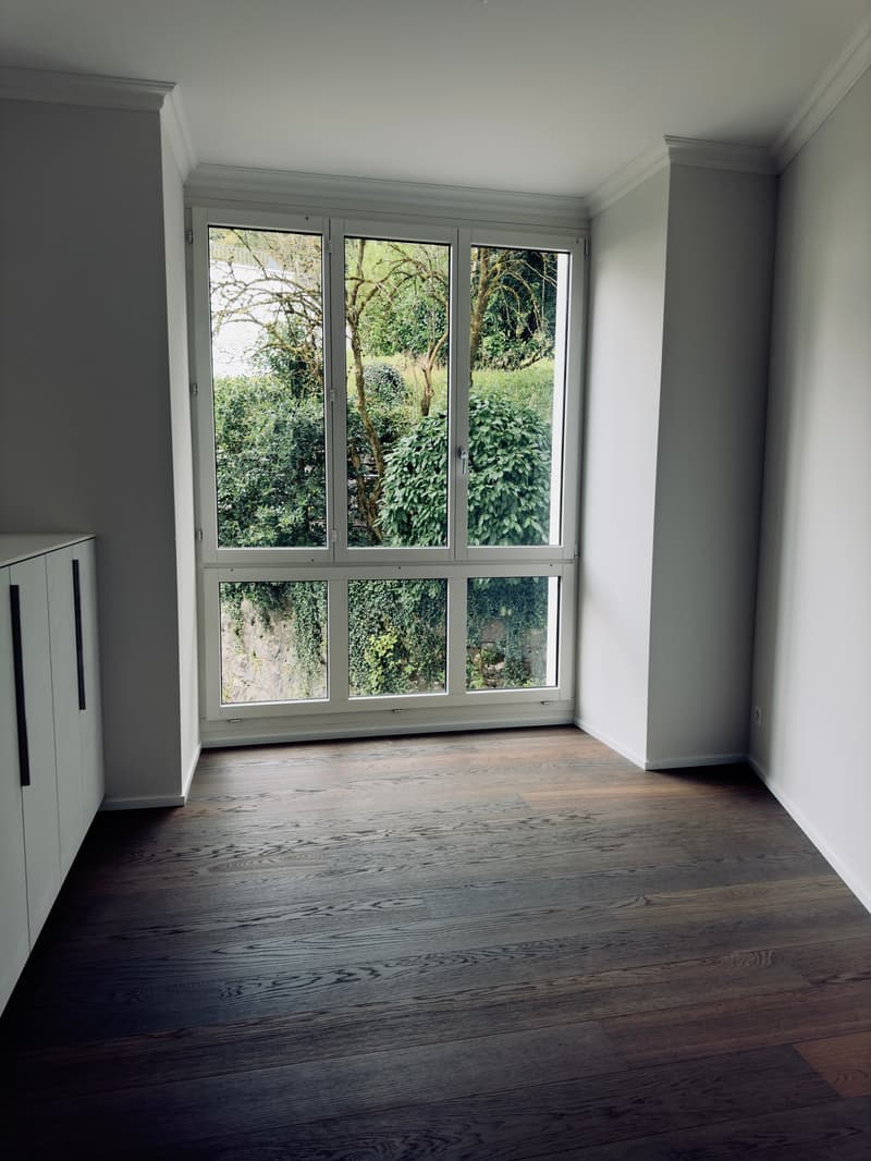 Empty room, wooden floor, glass doors and windows with trees view, white walls, white built-in cupboard, electrical outlet