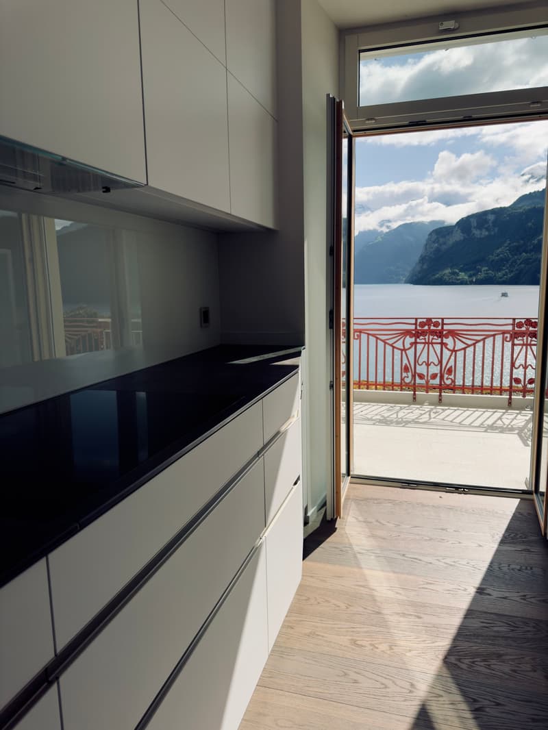 Modern kitchen with wooden flooring, white cabinets, black countertop, open door to balcony, lake view