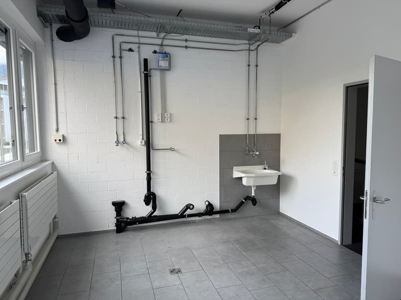 An empty room with white brick walls, gray tiled floor, a white sink, and a radiator.