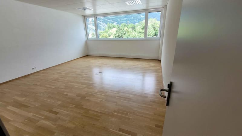 Spacious office room with large windows overlooking a scenic outdoor view, hardwood flooring, and minimal furnishings