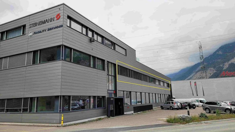 3-story commercial building with Steinemann Facility Services signage, large windows, and a parking lot in front of the building
