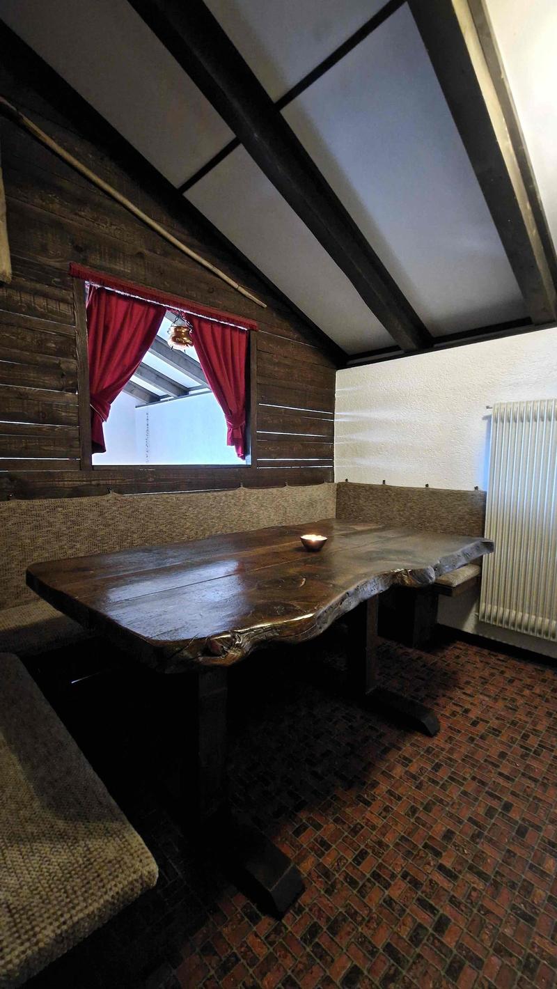 Wooden walls, window with red curtains, large wooden table, bench seating, central heating radiator