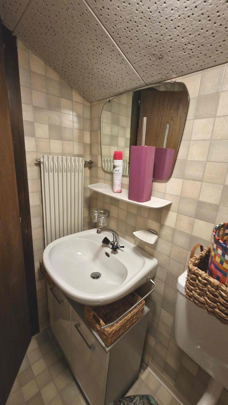 tiled walls, radiator, white sink, metal faucet, mirror with shelf, wicker baskets, toilet, air freshener, soap dispenser