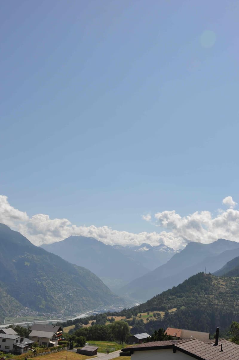 Mountains with a valley, river, and houses with blue sky and white clouds.