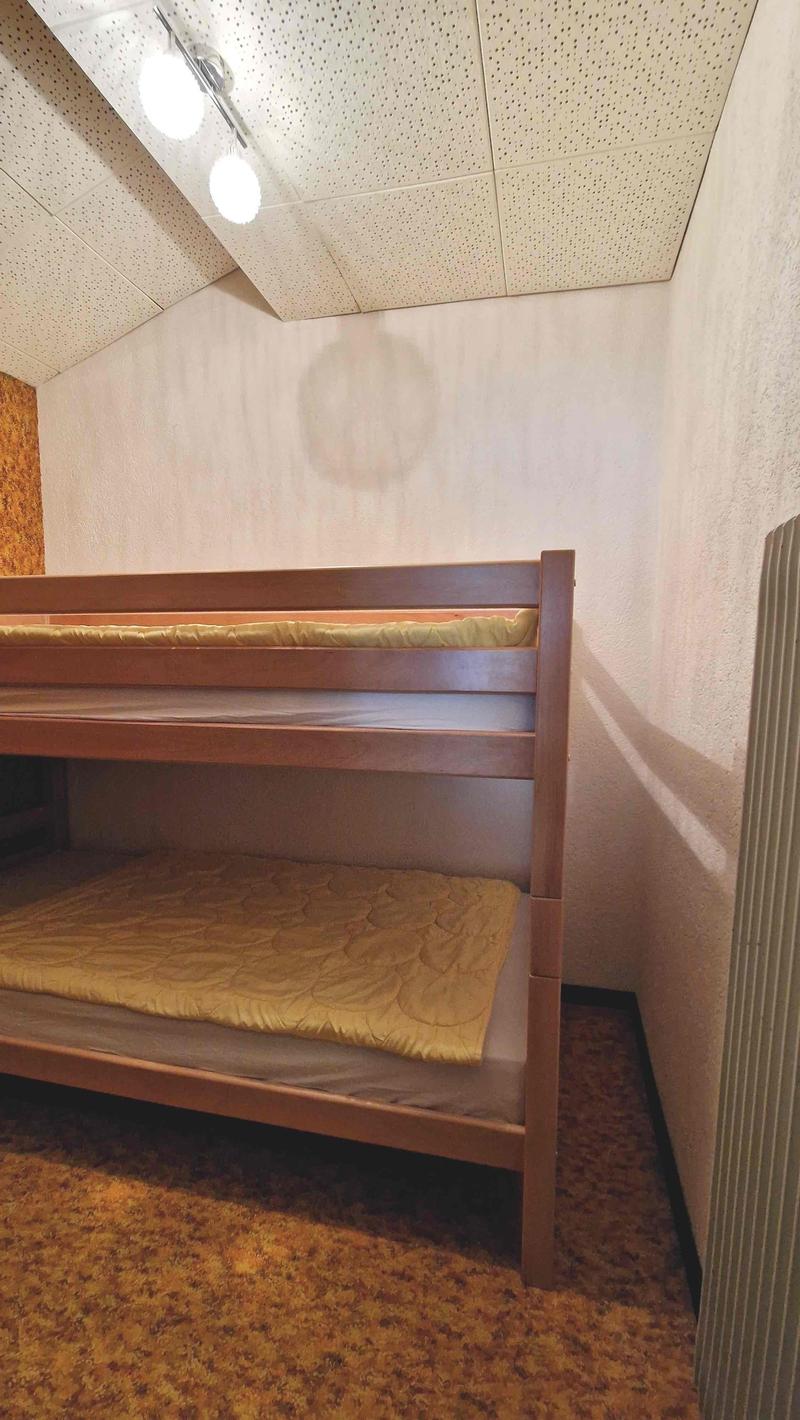 two-story wooden bunk bed, beige quilt, yellow mattress, beige carpet, white wall, beige ceiling, three lights