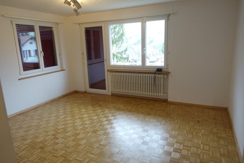 Spacious room with hardwood parquet flooring, large windows providing natural light, and a radiator along the wall.