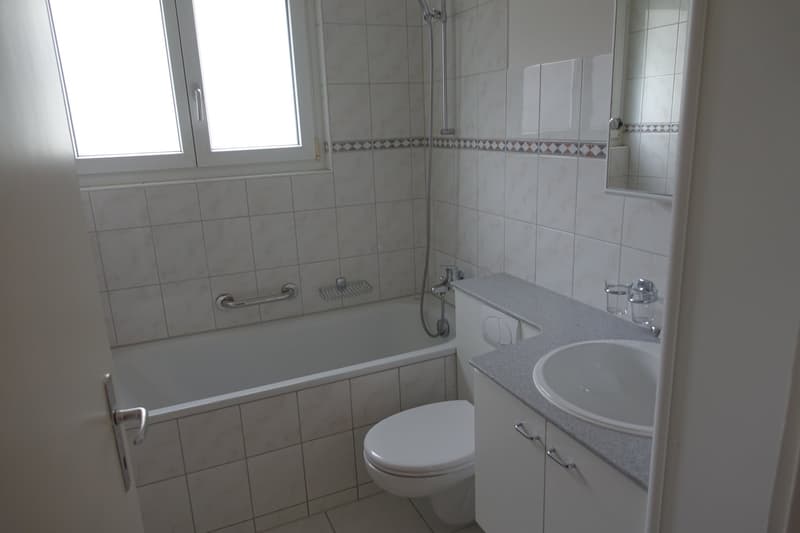 modern bathroom with bathtub, toilet, sink, white tiles, and a mirror