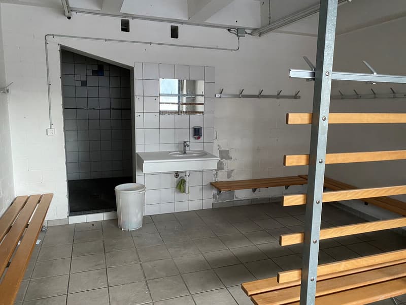 tiled floor, wooden benches, white sink with faucet, metal wall hooks, soap dispenser, trash bin, shower stall