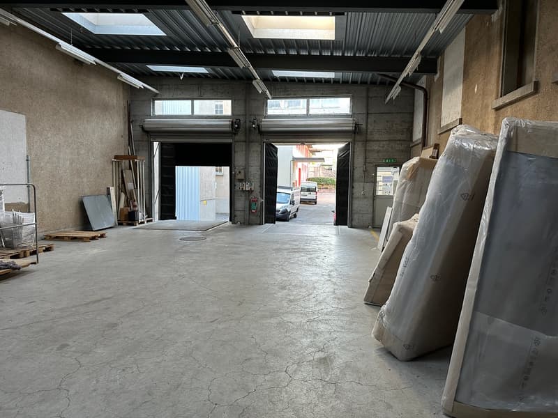 Wide open space, concrete floor, large garage doors, fluorescent lighting, two rows of pallets, two vehicles