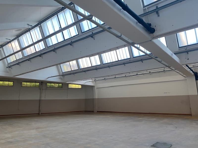 Empty room with white walls and ceiling, exposed beams, large windows, grey floor.