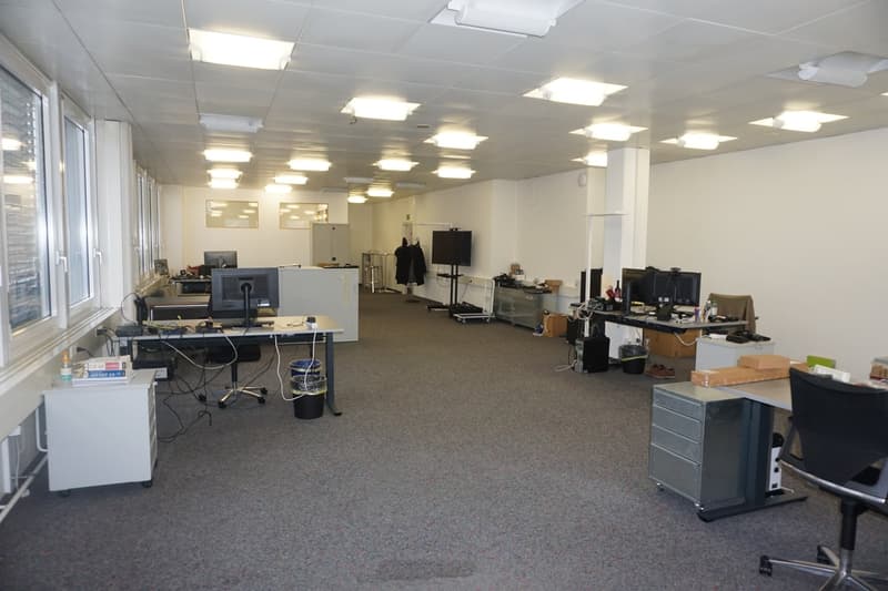 Large empty room with multiple desks, computers, chairs, trash bins, and storage boxes.