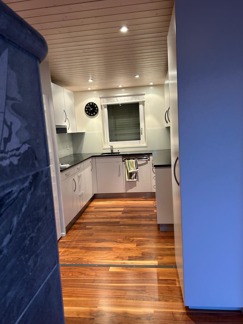 modern kitchen, white cabinets, wooden floor, black countertops, hanging towels, white tiles, ceiling lights