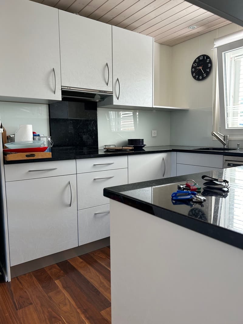 modern kitchen with black and white countertops, white cabinets, black oven, wooden floor, sink, faucet, and various kitchen items