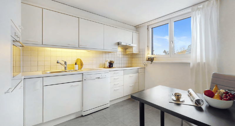 Bright and modern kitchen with white cabinets, yellow tile backsplash, dishwasher, and large window providing natural light