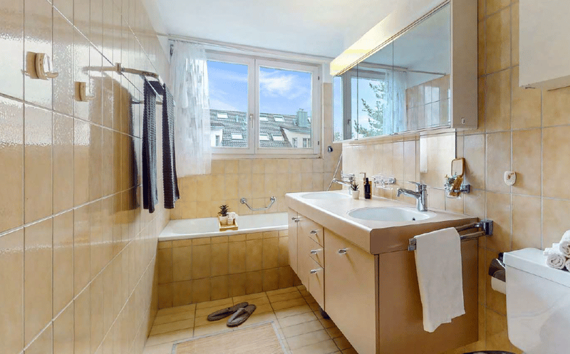 Spacious bathroom with large windows, tiled walls, bathtub, vanity sink, and towel rack.