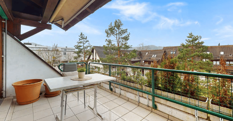Balcony with a small table and chairs, overlooking a residential neighborhood with trees and houses.