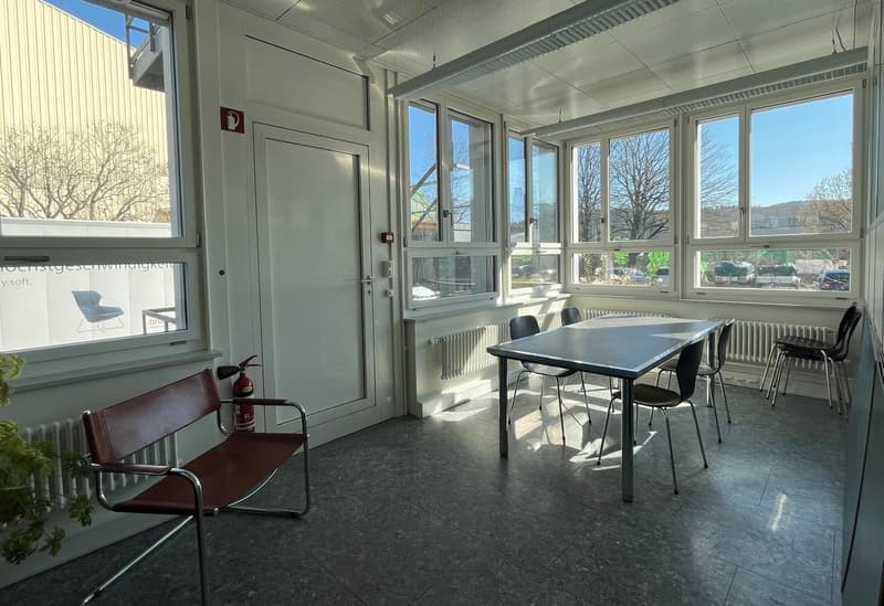 Spacious office with large windows, concrete floor, table and chairs, and a fire extinguisher on the wall