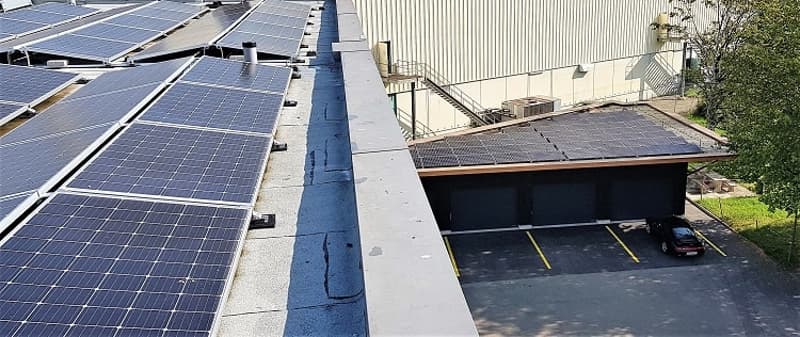 Large commercial building with a flat roof covered in solar panels. There is a parking area underneath the building.