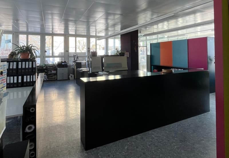 Large open office space with glass walls, black reception desk, computer equipment, and storage shelves