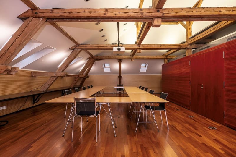 large meeting room, wooden desk, metal chairs, exposed wooden beams, projector, wooden floor, electrical outlet, red wall