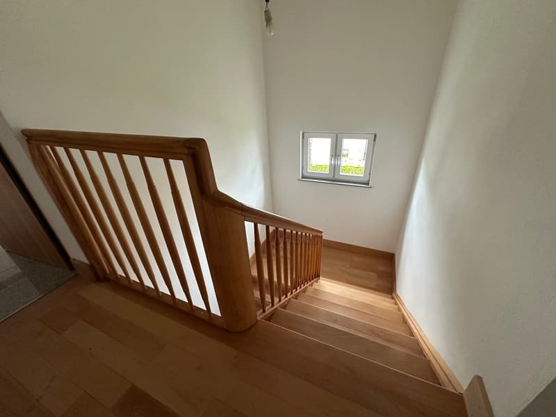 Wooden staircase with railing, leading to a window on the upper level