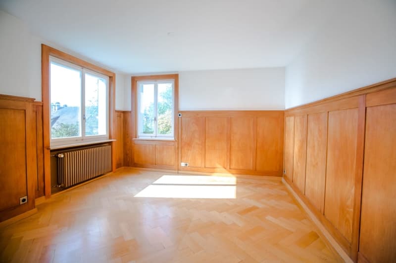 empty room, wooden floors, wooden paneled walls, windows with radiators