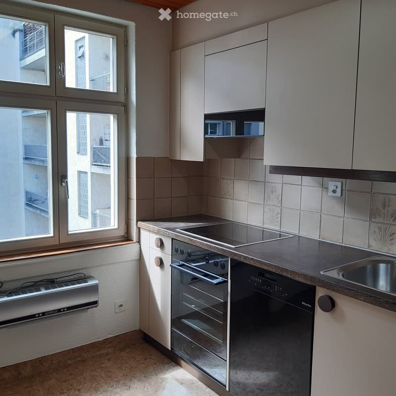Modern kitchen with white cabinets, black countertops, tiled backsplash, and built-in dishwasher and oven