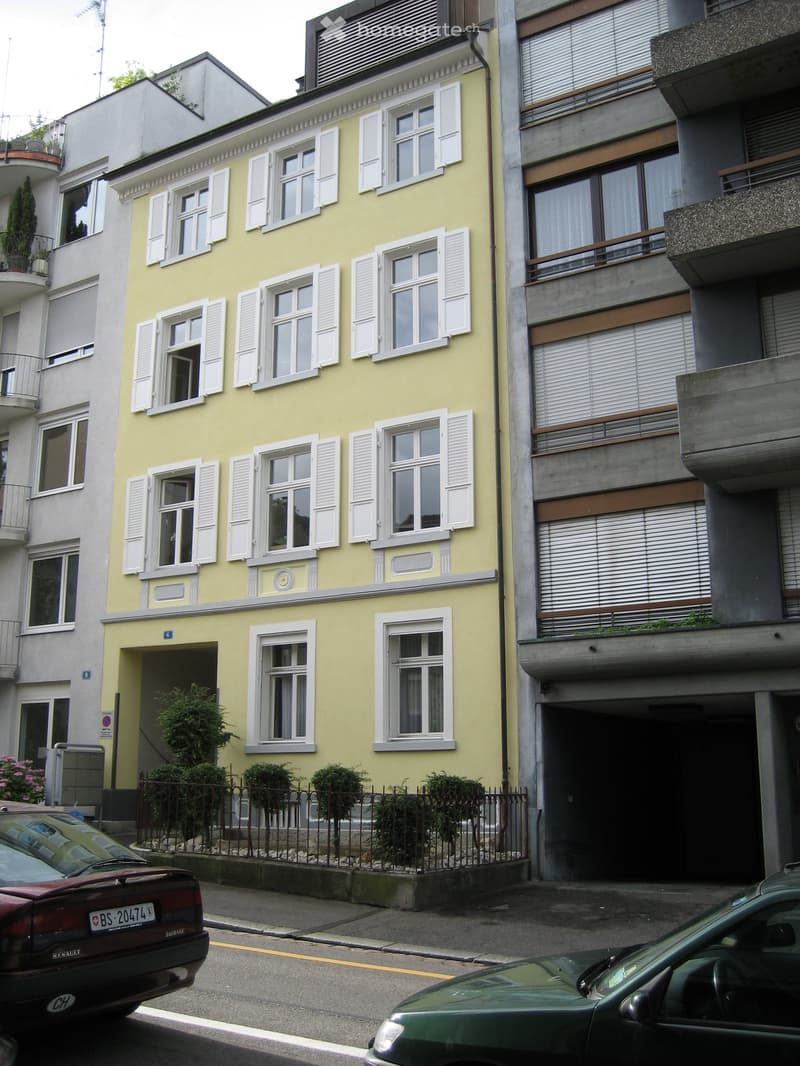 3-story yellow building with white shutters, balconies, and a garage on the ground floor