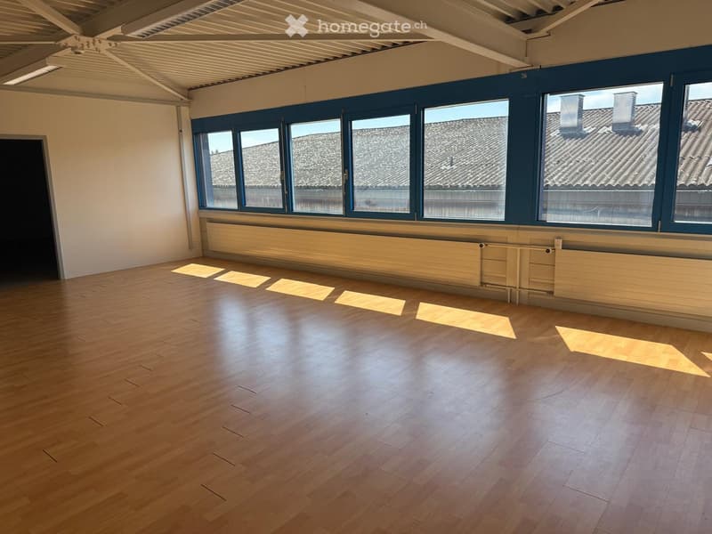 Large empty room with wooden flooring, windows, and radiators on the wall