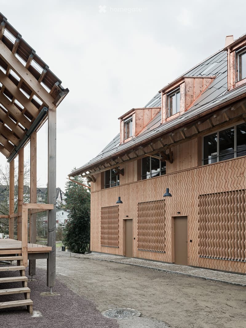 Wooden exterior, raised ground floor, slanted roof, windows, multiple doors, wooden deck with stairs