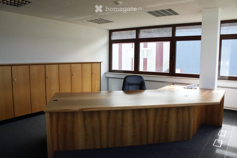 Large wooden desk, wooden cabinets, office chair, large windows providing natural light, tiled floor
