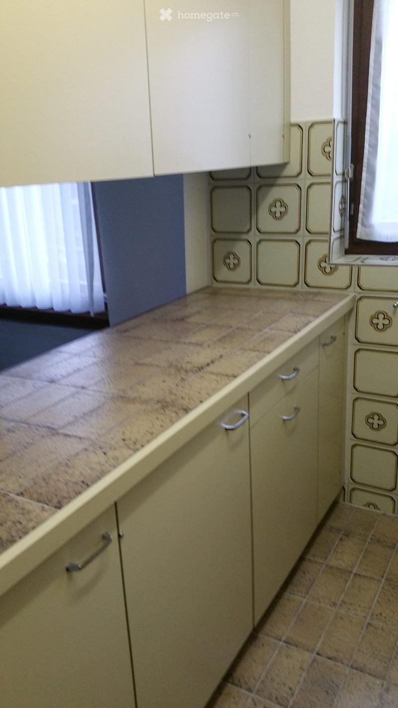 Beige cabinets with decorative floral patterns, granite countertop, tile flooring, window with curtains
