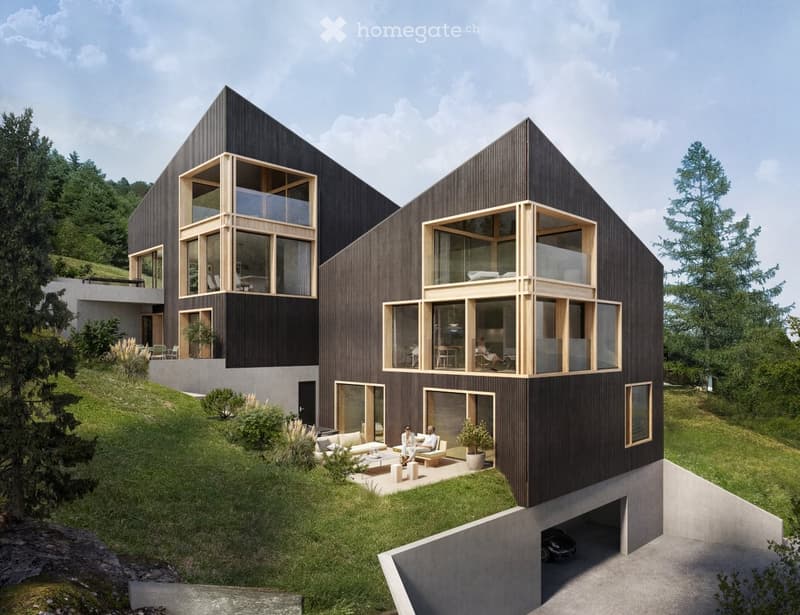 Two-story modern house with a unique angular design, featuring large windows and wooden accents. The house is situated on a grassy hill surrounded by trees. There is a garage visible on the ground level.