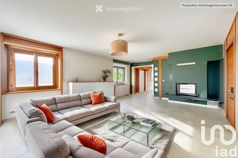Spacious open-plan living room with large windows, grey sectional sofa, orange accent pillows, glass coffee table, and a built-in entertainment unit with a TV. The room has a modern and cozy feel.