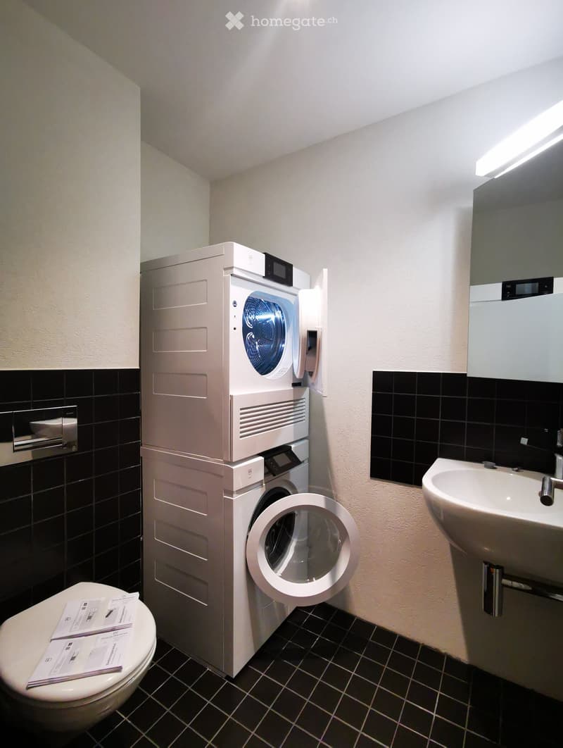 Bathroom with a washing machine and dryer unit, a sink, and a toilet. The room has black and white tile flooring.