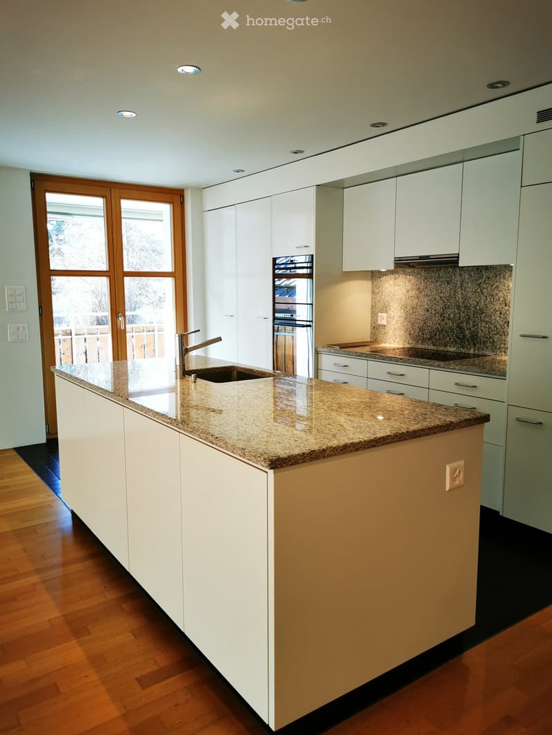 Modern kitchen with white cabinets, granite countertops, stainless steel appliances including a dishwasher, and large windows providing natural light.