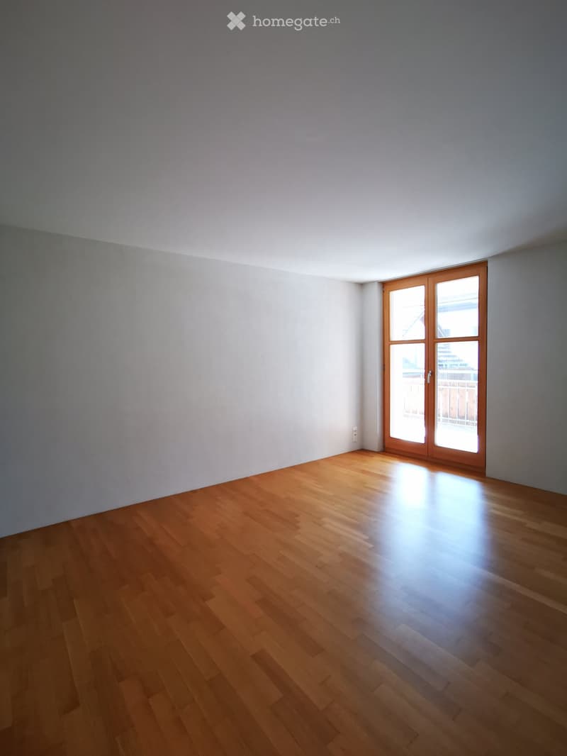 Empty room with white walls, hardwood floor, and a large window with wooden frame.
